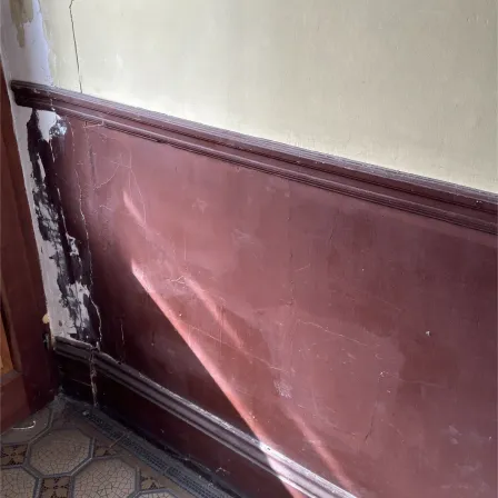 Soubassement peint en bordeaux dont la peinture s'écaille largement, dans la cage d'escalier d'un immeuble ancien