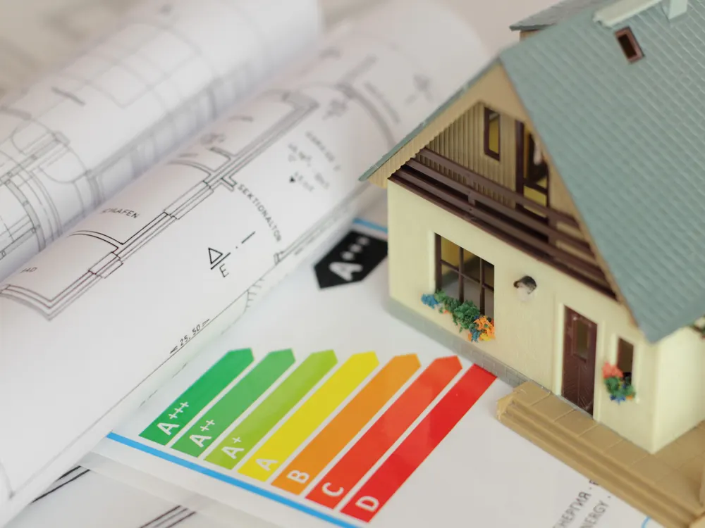 Plans d'architecte enroulés, maquette de maison et étiquette énergie colorée posés sur une table