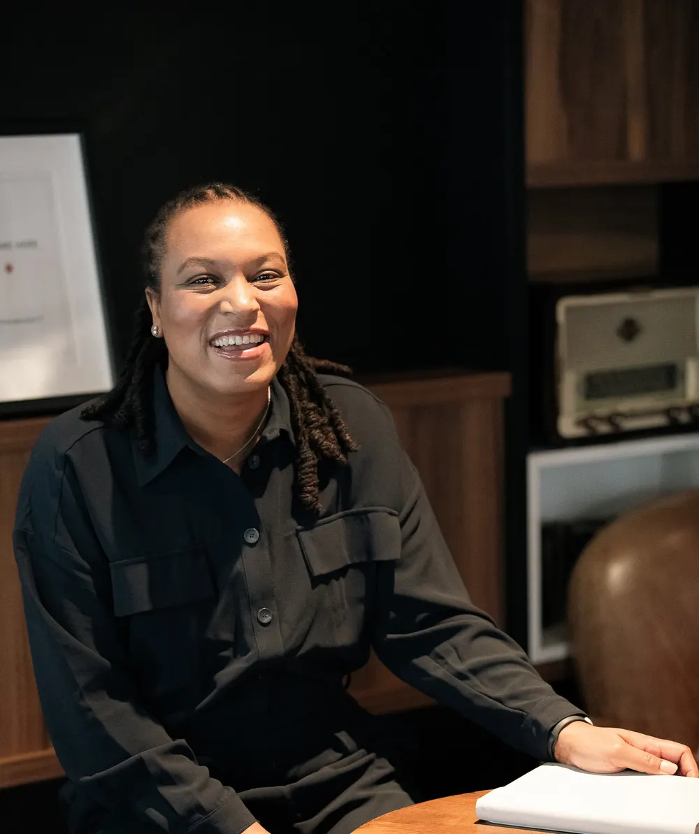 Marie-Sully Biabiany, souriante, assise à une table de travail dans un intérieur sombre