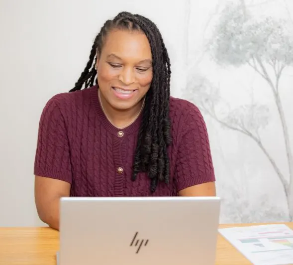 Marie-Sully Biabiany travaille en souriant devant un ordinateur portable, des documents imprimés posés à côté