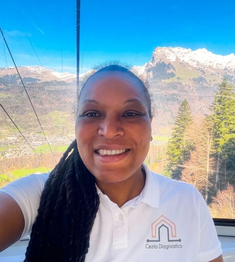 La diagnostiqueuse en polo Cezia Diagnostics, en déplacement, dans une cabine de téléphérique face à un paysage de montagne enneigée
