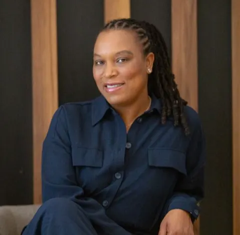 Portrait de Marie-Sully Biabiany assise dans un fauteuil, devant un mur de lattes de bois