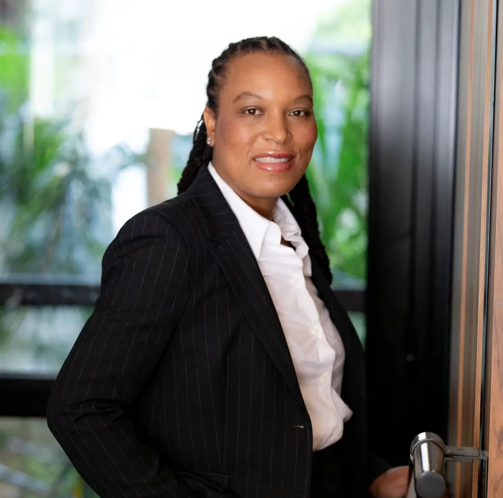 Portrait de Marie-Sully Biabiany en costume, la main posée sur la poignée d’une porte vitrée